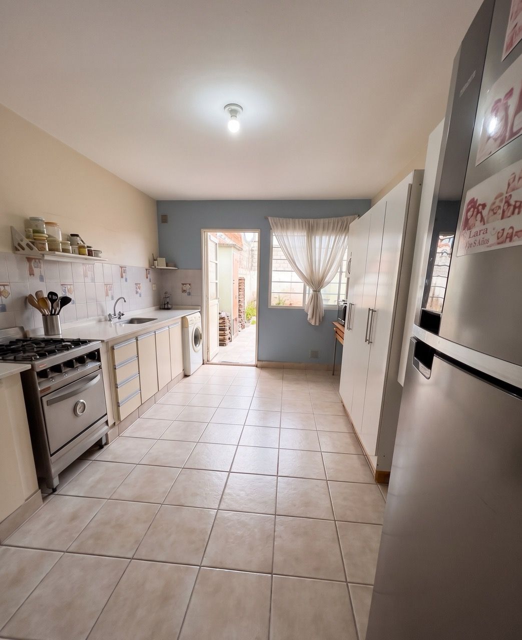 Cocina larga con cocina a gas, mesada, lavarropas y puerta que da al patio