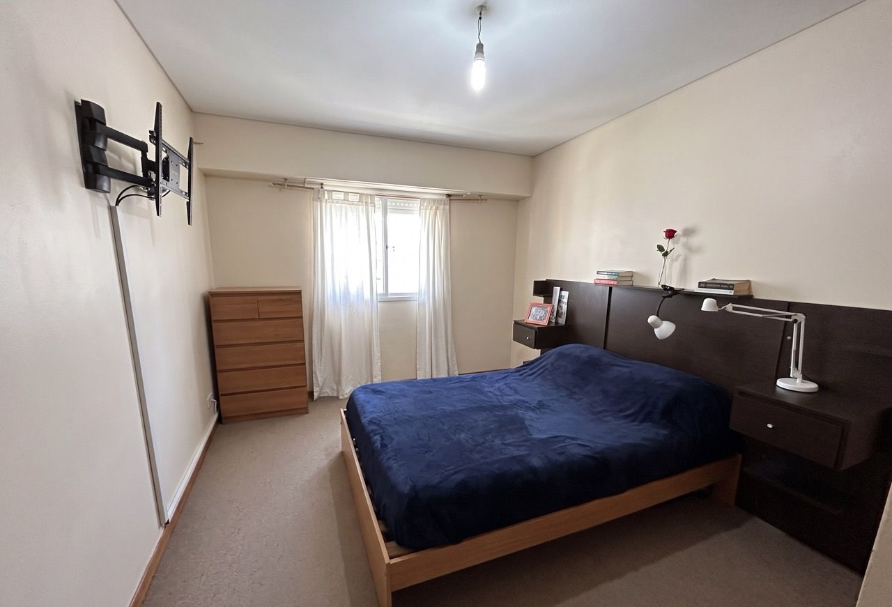Dormitorio con cama de dos plazas, cómoda de madera y ventana con cortinas blancas