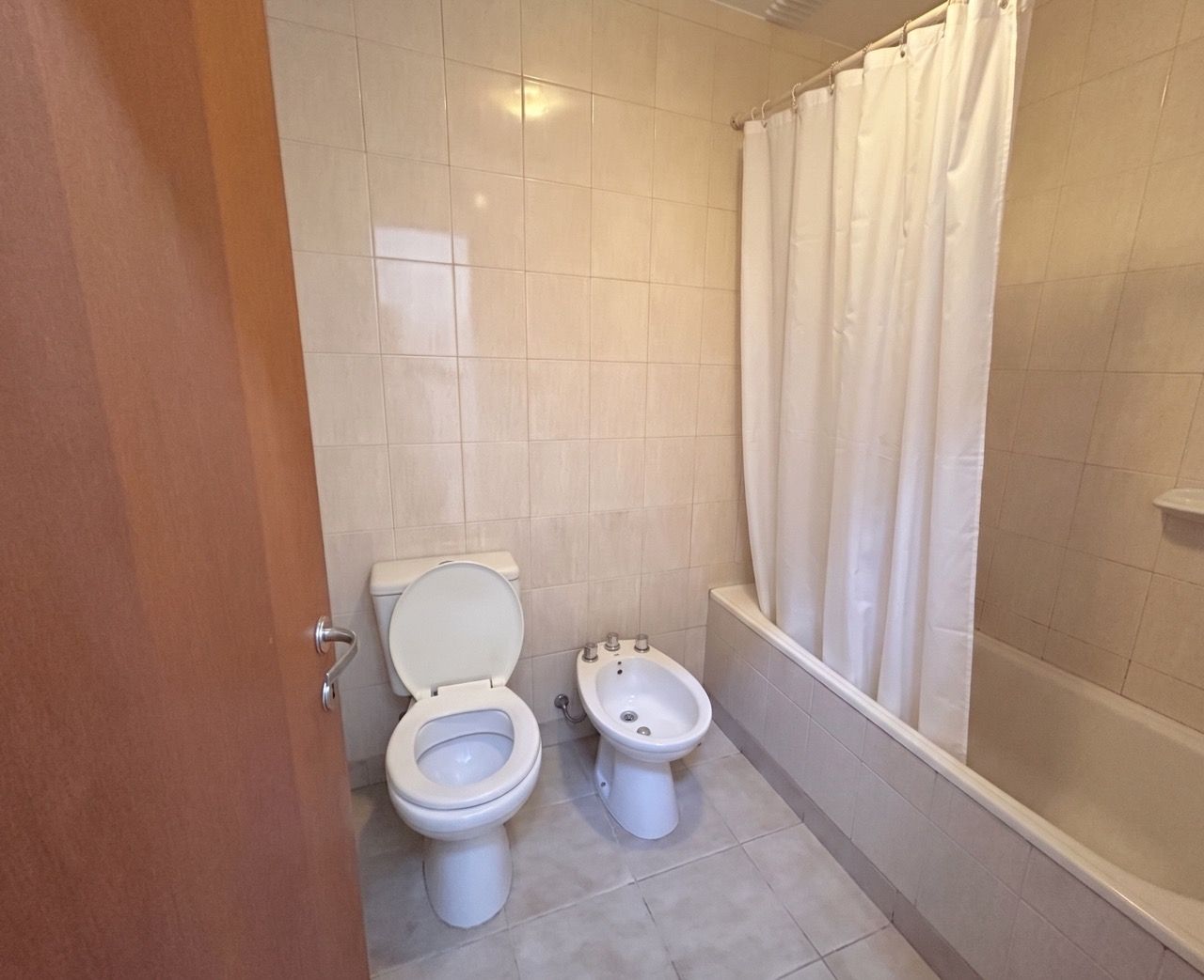 Baño completo con inodoro, bidet y bañera con cortina blanca