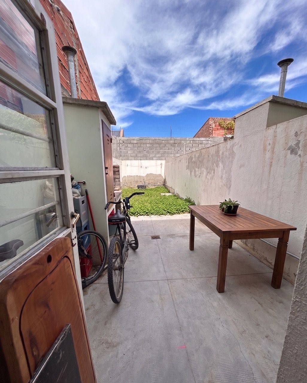 Patio lateral con una mesa de madera y dos bicicletas apoyadas contra la pared