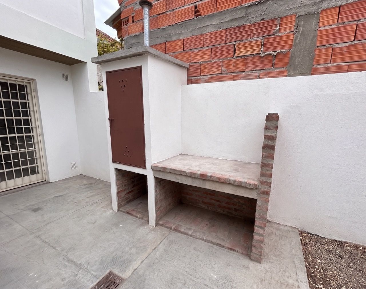 Fogón de ladrillo con mesada de cemento y paredón blanco en el patio