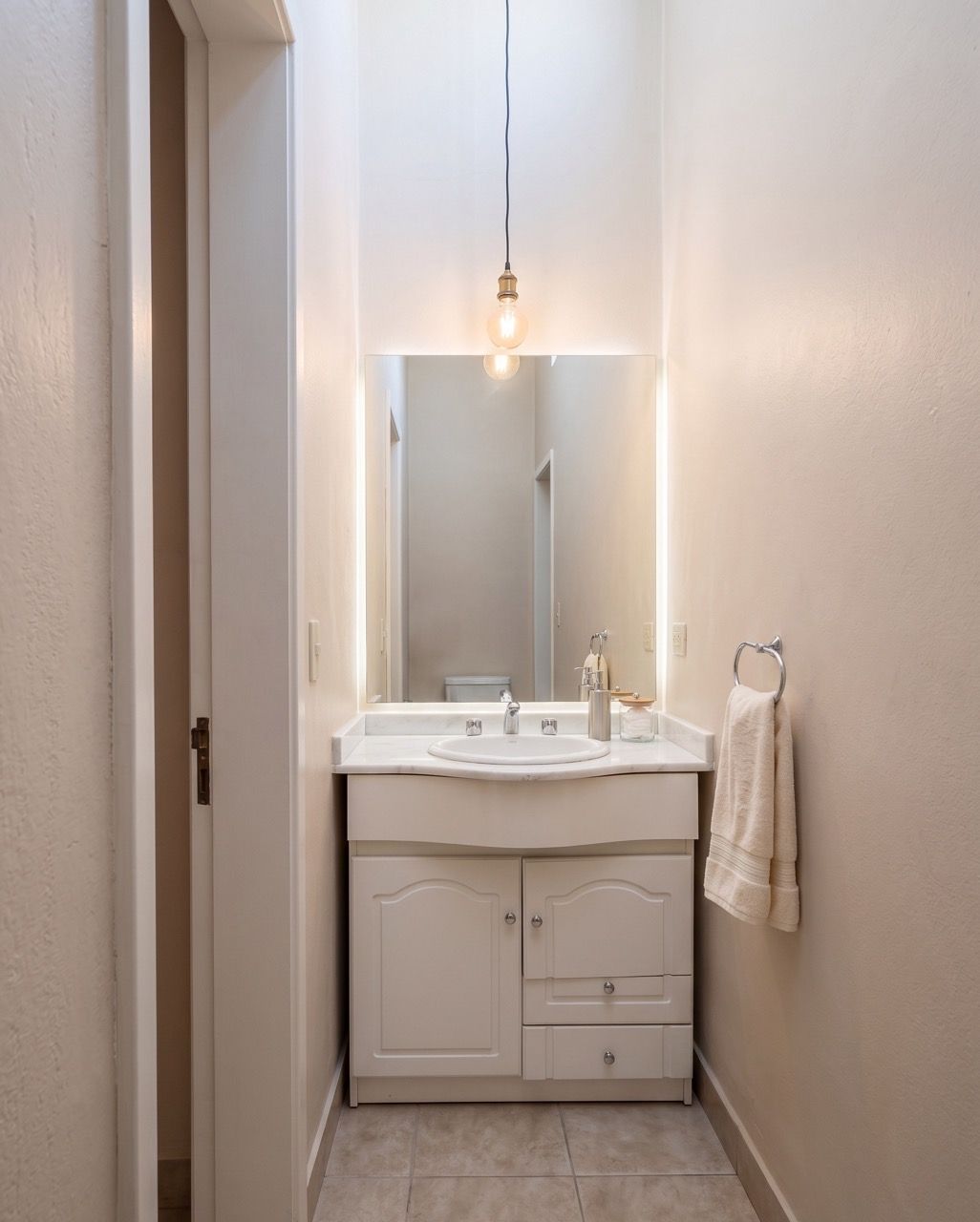 Toilette con mueble bajo mesada, espejo con luz y una lámpara colgante